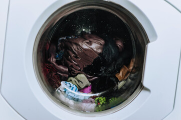 Wet dirty clothes are washed in a washing machine inside with water behind a glass round porthole. Close-up photo, washing.