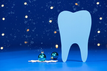 Christmas dentistry - a tooth on a blue background with balls and bokeh garlands, a place for text.