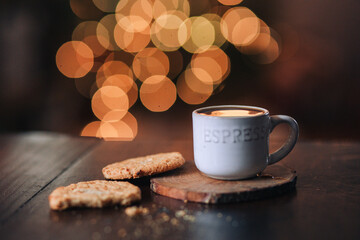 cup of coffee and cookies on dark table with glittering lights background