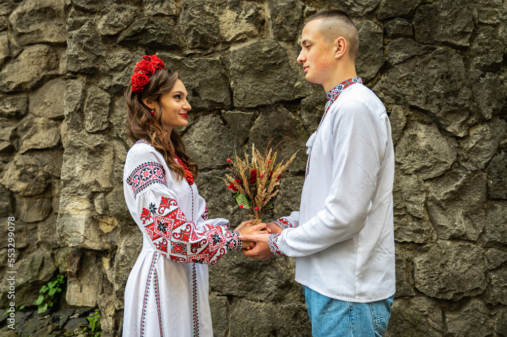 Wall mural A young, emotional, happy couple in love, a family walks through the old city of Lviv in Ukrainian embroidered shirts, holding hands against the background of the old city. Young people hug in the old