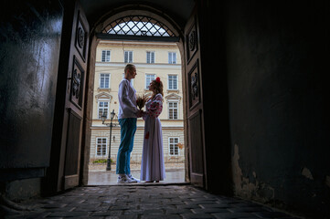 Fototapeta na wymiar Profile view of a young couple in love in Ukrainian national dress in an embroidered shirt embracing while standing in a doorway. View from the corridor through the doorway. Creating a family