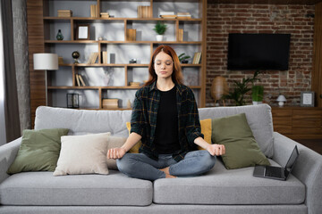 Calm of caucasian young woman doing yoga lotus pose to meditation and relax on couch during work...