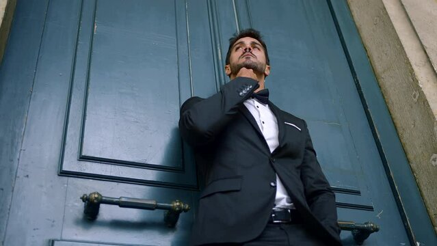 Young man with beard and in suit stands attractively against wall. Action. Elegant hot man in suit against wall. Rich man in sexy suit stands like model