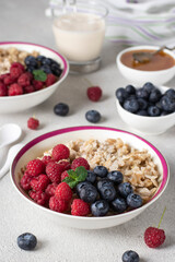 Oatmeal porridge with blueberries, raspberry and honey on light gray background. Breakfast meal concept