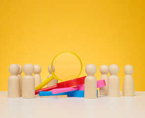 Wooden figures of men stand on a yellow background and a plastic magnifying glass. Recruitment concept