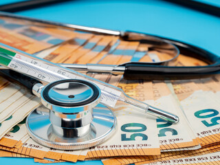 Medical stethoscope, thermometer and banknotes on a blue background.