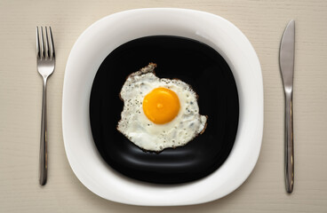 Fried eggs on a black and white plate with serving at a white table