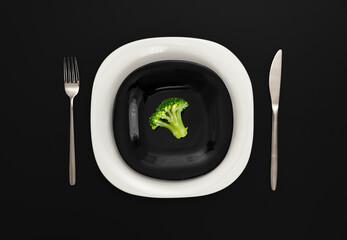 A small portion of boiled broccoli on a black and white plate with a knife and fork on a black...