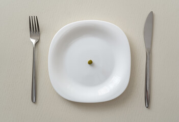 A small pea on a white plate on a white table with a knife and fork, minimum calories