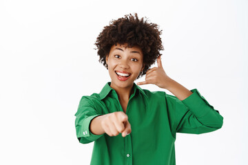 Smiling girl showing phone and pointing at you, call us gesture, callcenter advertisement, contact us, standing over white background