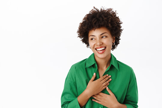 Portrait of young happy african american woman laughing, pointing at herself and looking pleased, standing over white background
