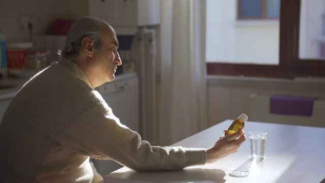 Elderly sick man looking at medicine bottle in kitchen at home.
Old man thoughtful about his illness looking at his meds and feeling helpless.
