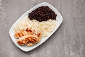 Healthy food with chicken breast, beans and rice on a white plate.