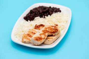 Healthy food with chicken breast, beans and rice on a white plate.