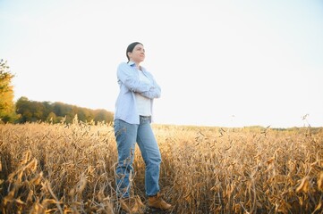 Portrait of young female farmer standing in soybean field examining crop.
