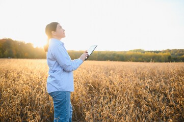 Portrait of young female farmer standing in soybean field examining crop.