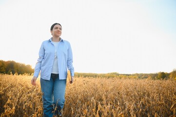 Naklejka na ściany i meble Portrait of young female farmer standing in soybean field examining crop.