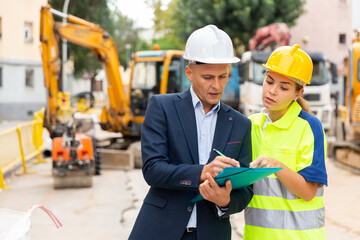 Foreman in suit and white hardhat discussing project documentation while staning in cosntruction...