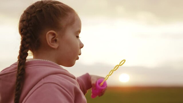 child blowing soap bubbles sunset. kid plays by inflating large transparent balloons. soap game kindergarten. chidhood dream. girl daughter evening plays with soap bubbles against sky. happy family.