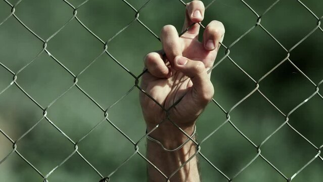 hand of a young man clinging to the net behind wich he is helded prisoner 