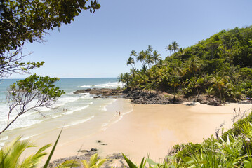 Beautiful paradise beach with coconut trees, clear water, rock formations and people bathing in the sea on a beautiful blue sky day