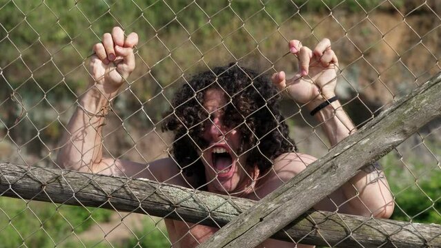 young prisoner with his hands clinging to the net screams