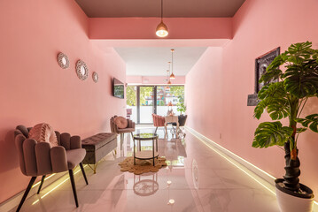 Waiting room of a beauty salon with gray velvet seats, circular coffee table and solid pink painted walls