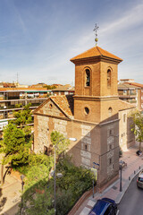 Fototapeta na wymiar A neighborhood church in Madrid, Spain, with a mud brick bell tower between the buildings and surrounded by trees