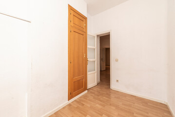 Empty room with oak imitation wood flooring, white painted solid wood doors with glass windows and a narrow built-in wardrobe with a trunk