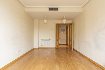 An empty room with double wooden doors, an aluminum radiator, air conditioning through hidden ducts in the false ceiling and oak parquet floors.