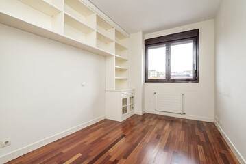 An empty room with a white lacquered wooden tall bookcase with a low cabinet and a reddish parquet floor