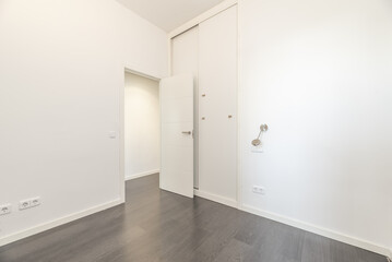 An empty room with smooth white walls, a floor-to-ceiling built-in wardrobe with sliding doors and gray wooden floors