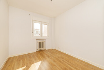 An empty room with plain white walls, oak laminate flooring, niche with cast iron radiator below aluminum thermal break window