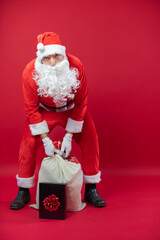 Portrait von einem verkleideten Weihnachtsmann mit Geschenk, isoliert auf roten Hintergrund im Studio im Hochformat