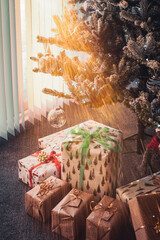 Presents wrapped under a Christmas tree as sun rays shine through vertical blinds on patio doors next to the tree.