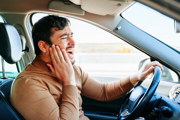 Side view young male driver holding on to the tooth while sitting in the car. Neuralgia and...