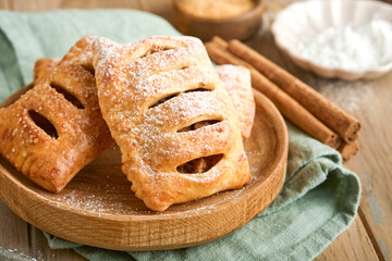 Hand pies. Mini puff pastry or hand pies stuffed with apple and sprinkle sugar powder in wooden plate. Homemade pie snack with crust for breakfast rustic photo.  Copy space.