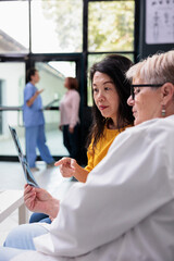 Senior physician doctor looking at radiography exam scan with asian patient. Specialist explaining healthcare treatment during appointment in hospital waiting area, medicine concept