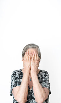 Senior woman covering her face with her hands deformed because of rheumatoid arthritis. Isolated white background.