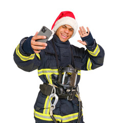 Young smiling african american firefighter in uniform and red santa claus hat holding smartphone in hand and taking selfie isolated on white background