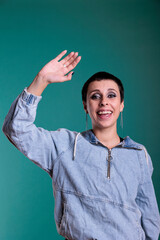 Smiling happy woman waving with palm at camera having fun in studio, person being friendly. Cheerful female doing salute gesture to greet people whle standing over isolated background