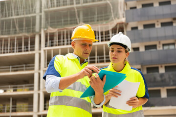 Man and a woman working at a construction site discuss a construction plan, holding an estimate in their hands