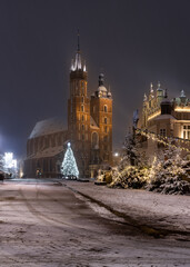 Fototapeta premium Krakow, Poland, snowy Main Market square, St Mary's church and Cloth Hall in the winter season, during Christmas fairs decorated with Christmas tree
