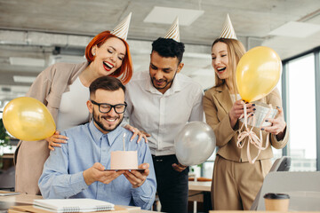 Young man is going to blow candles on cake and make a wish while celebrating birthday with colleagues. Colleagues celebrating a birthday in the office