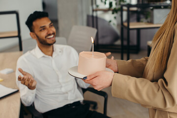 A young Hindu man is about to blow out candles on a cake and make a wish during a birthday celebration with colleagues. Colleagues celebrate a birthday in the office
