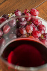 Glass of fine red wine and bunch of fresh grapes on a white plate and wooden table.