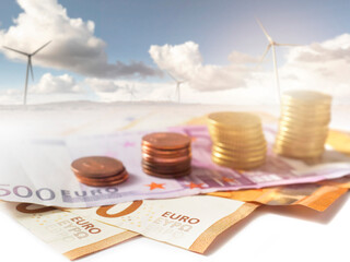 Euro banknotes and coins. Field with wind farm out of focus in the background. Investment in green...