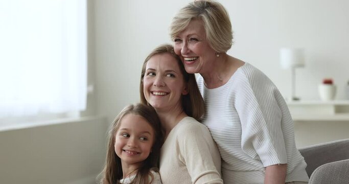 In row of three generation of women, 60s middle-aged, senior grandmother, grown up daughter, young mother, little granddaughter posing together indoor. Multi-generational happy female family portraits