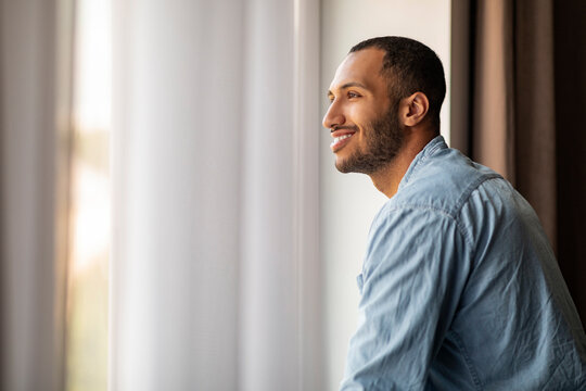 Handsome Smiling African American Guy Standing Near Window At Home