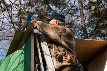 senior man in a ladder framing an hunter shack with the help of a friend